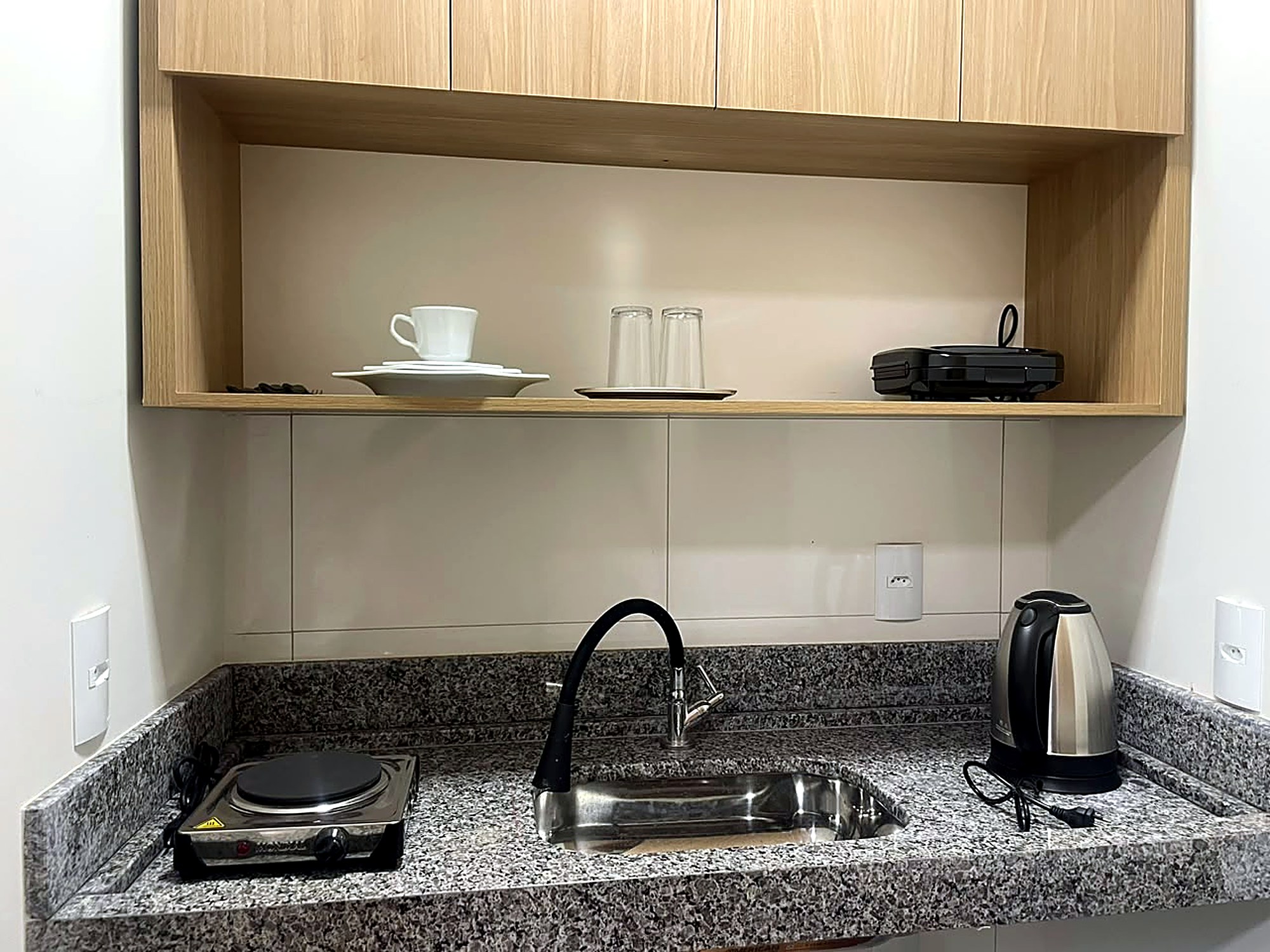Cozinha equipada do flat, com cooktop e bancada de granito